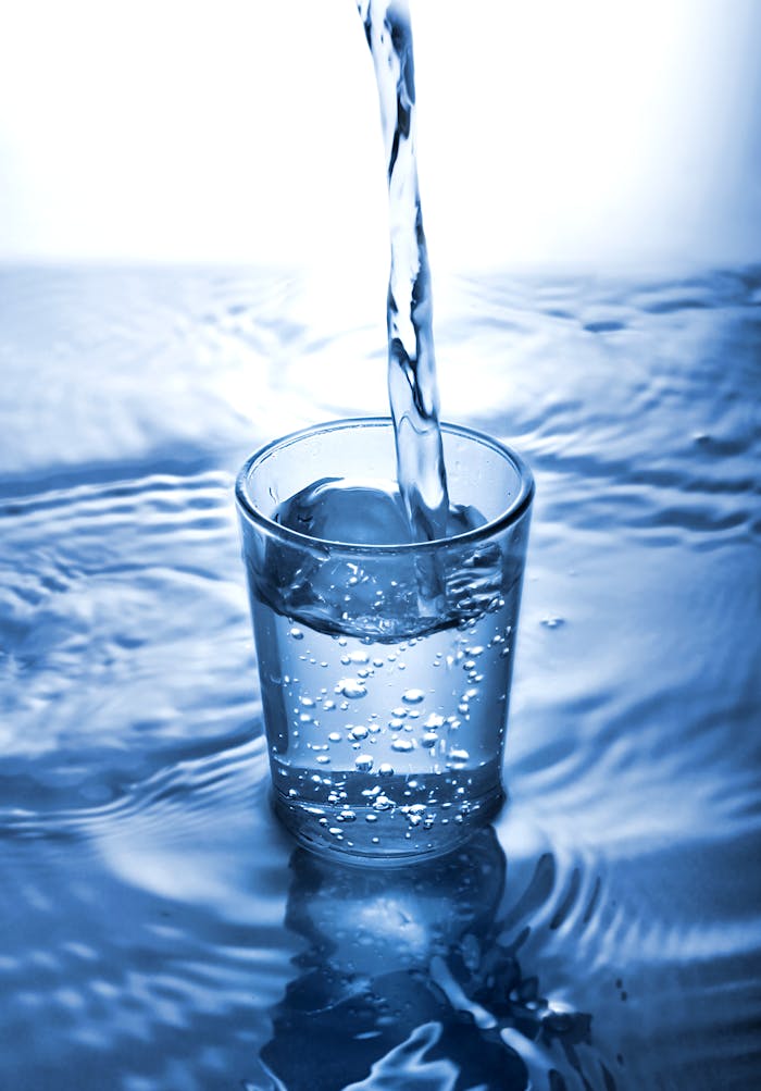 A vertical shot of water pouring into a glass, creating ripples in a serene blue setting.